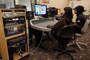 Students seated at a sound board control room.